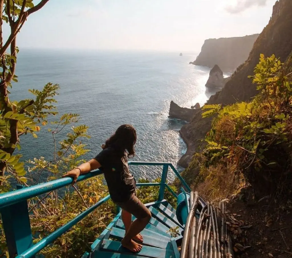 Pemandangan birunya laut berpadu dengan langit yang bersih dan tebing hijau di Air Terjun Peguyangan Klungkung Bali