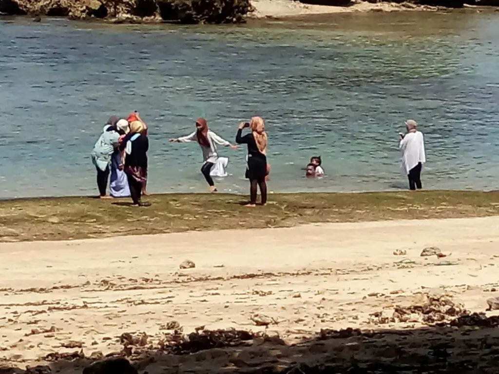 Wisatawan sedang bernenang di area tepi pantai