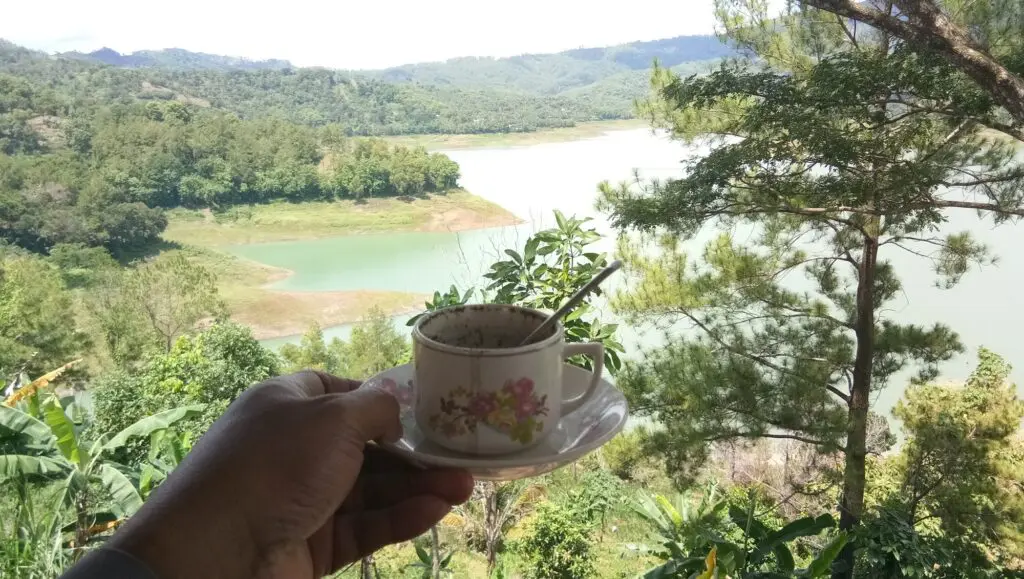 Secangkir kopi dengan latar panorama danau