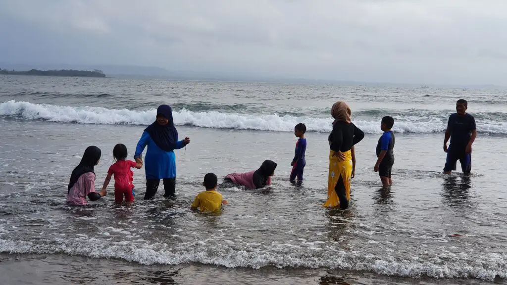 Pengunjung berenang di tepi pantai bersama keluarga