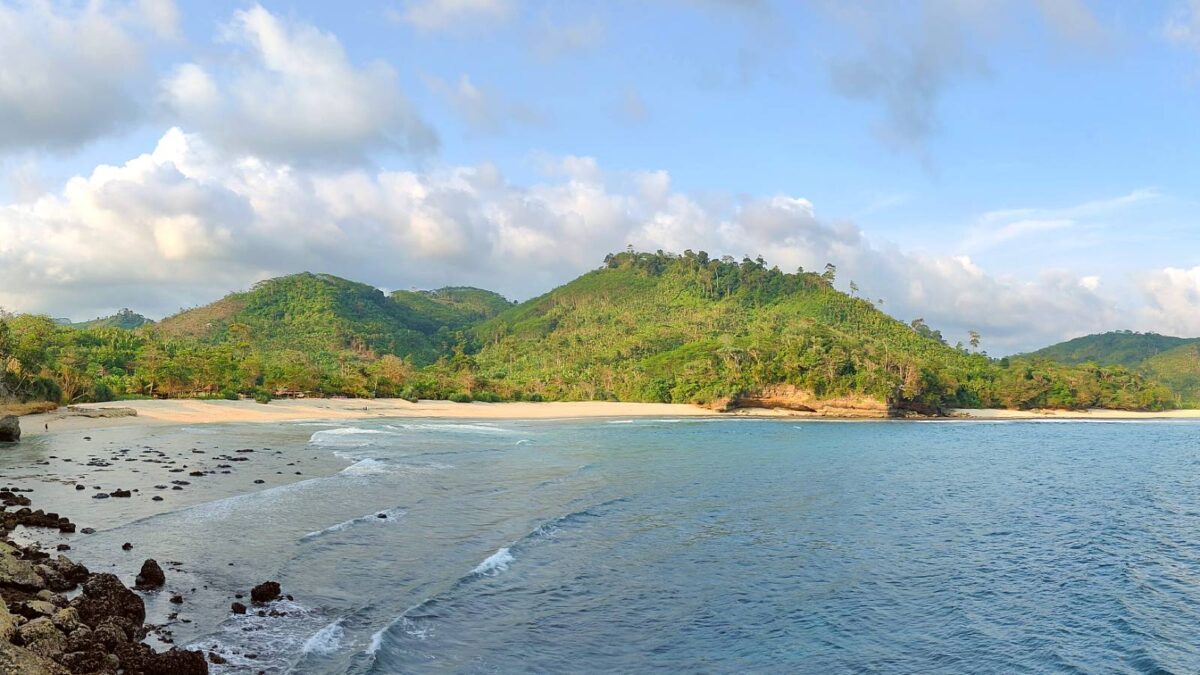 kawasan sekitar pantai sanggar dengan laut biru dan perbukitan hijau