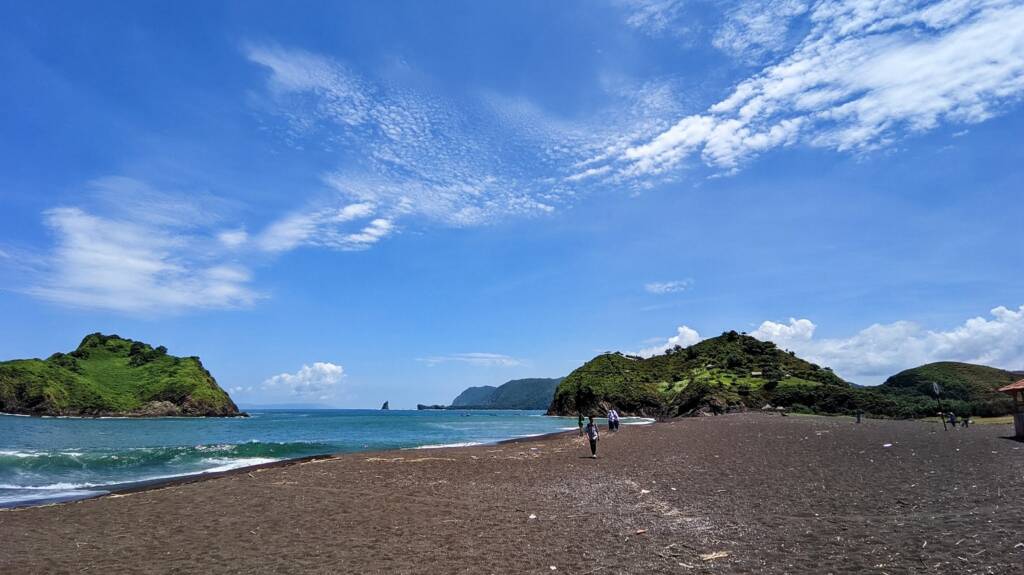 area tepi pantai dengan laut biru dan perbukitan hijau di pantai peyangan