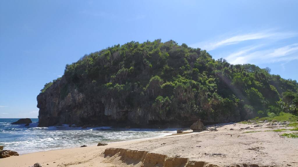 Pantai Kayu Arum dengan pasir putih dan bukit karang di sisinya
