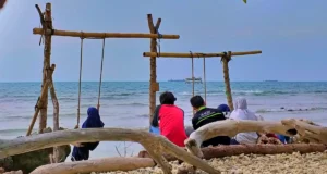 wisatawan bermain ayunan sambil bersantai di tepi Pantai Munir
