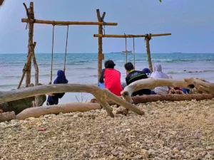 wisatawan bermain ayunan sambil bersantai di tepi Pantai Munir