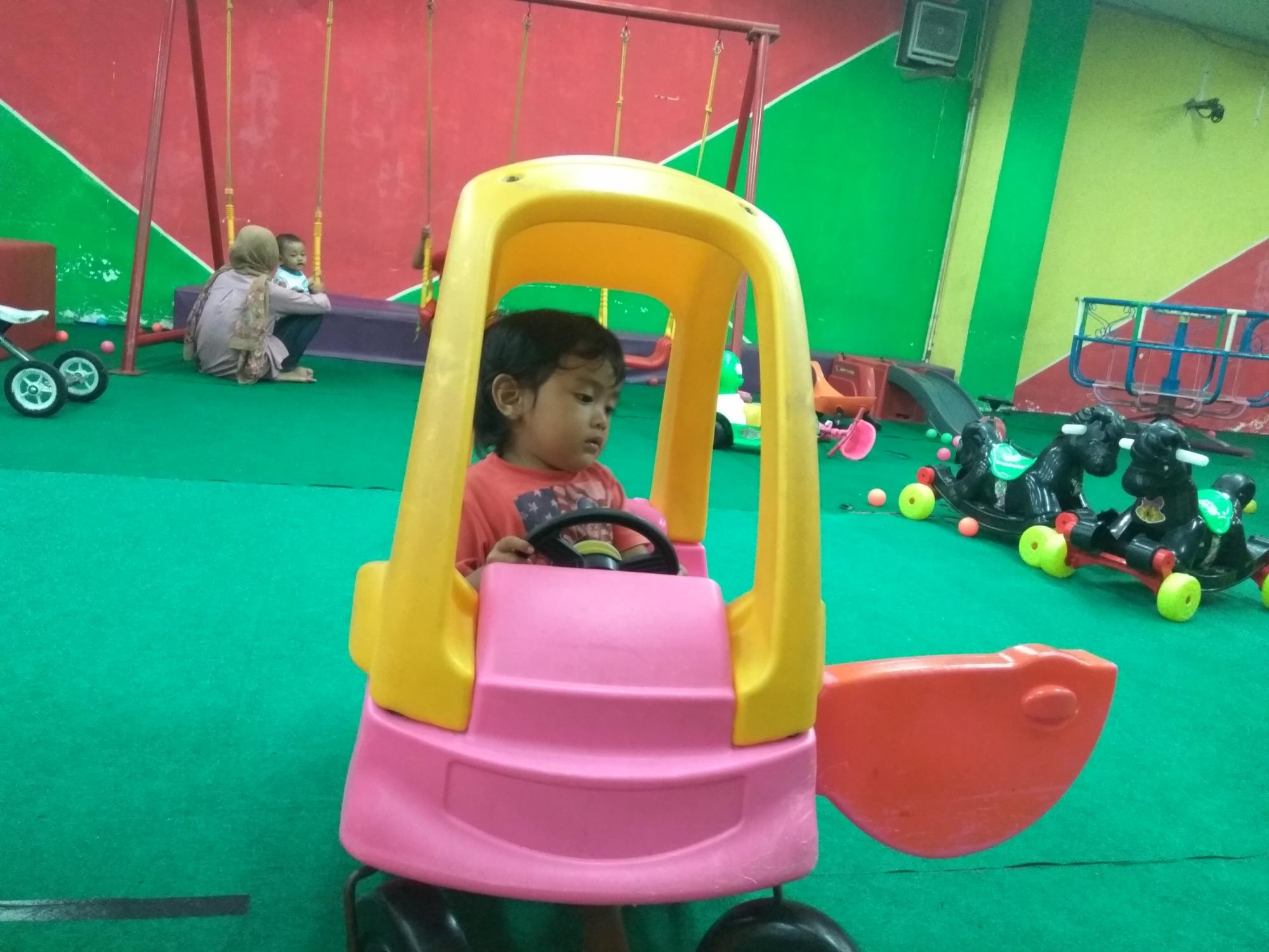 Anak perempuan tengah mengendarai mobil mainan.