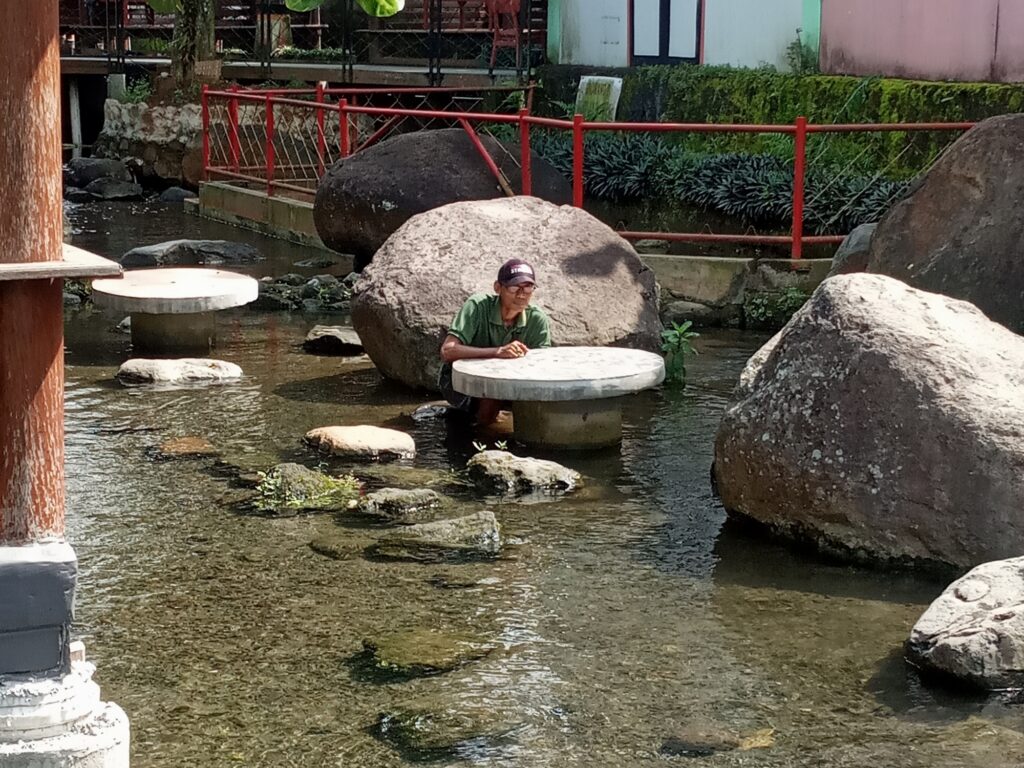 Seorang pria duduk di atas batu di sebuah kolam kecil.
