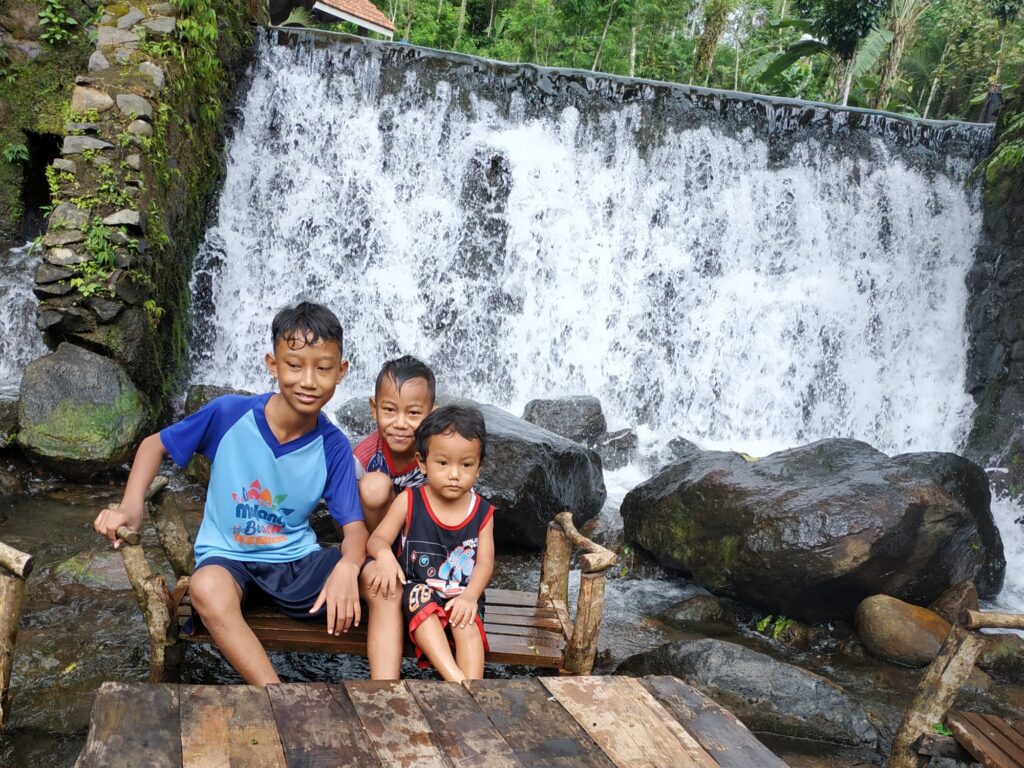Tiga Anak berfoto di depan air terjun buatan Wisata Umbul Tanaka.