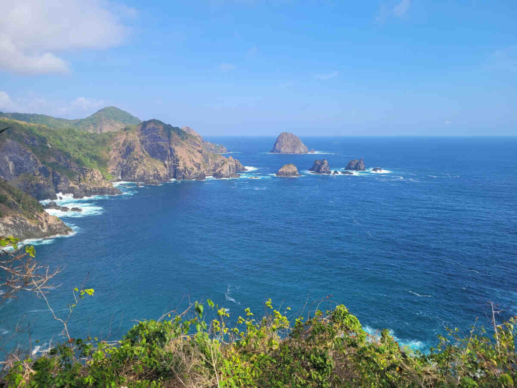 lanskap pantai Orong Bukal dengan laut biru dan tebing batu